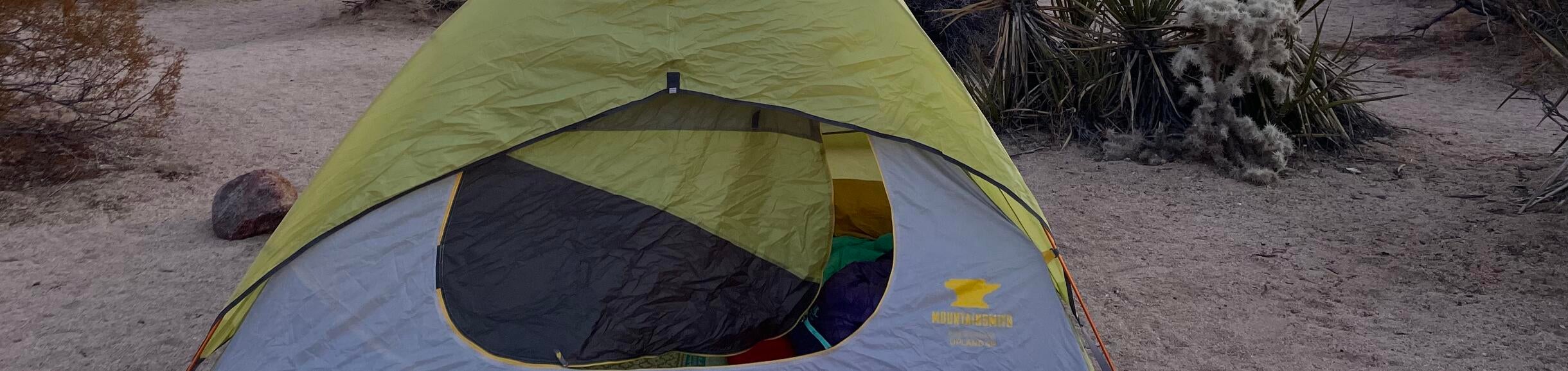 A tent sits set up with its door open and sleeping bags inside at sunset